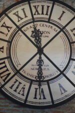 A large vintage industrial clock featuring a rustic design with bold numerals and exposed gears. The clock combines a weathered frame with metal accents, giving it a distinctive industrial look that adds character to any room.