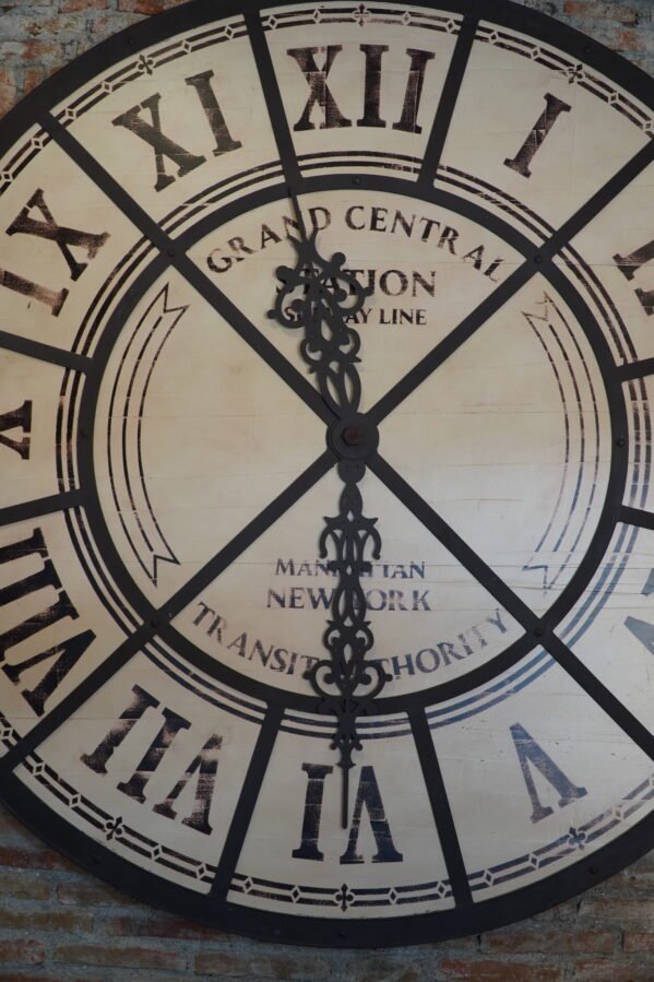 A large vintage industrial clock featuring a rustic design with bold numerals and exposed gears. The clock combines a weathered frame with metal accents, giving it a distinctive industrial look that adds character to any room.