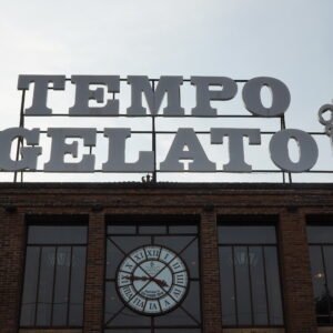A large vintage industrial clock made of wood and metal, featuring a rustic design with bold numerals and exposed gears. The clock combines a weathered wooden frame with metal accents, giving it a distinctive industrial look that adds character to any room.